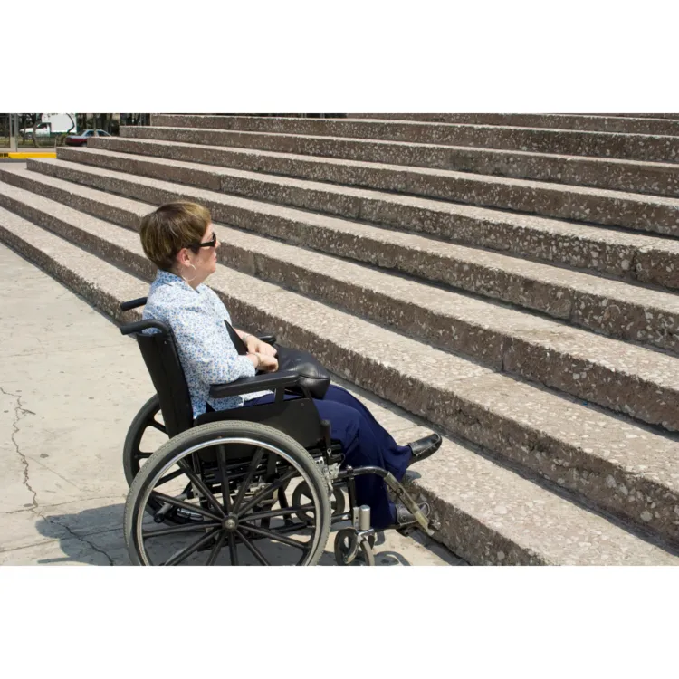 Person in wheelchair facing stairs with no accessible ramp.